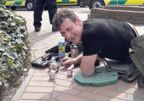 Ben Wilson painting a message on chewing gum outside the Whittington Hospital