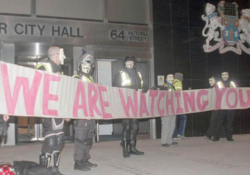 Biker protesters wearing masks unfurl their CCTV parking campaign banner outside